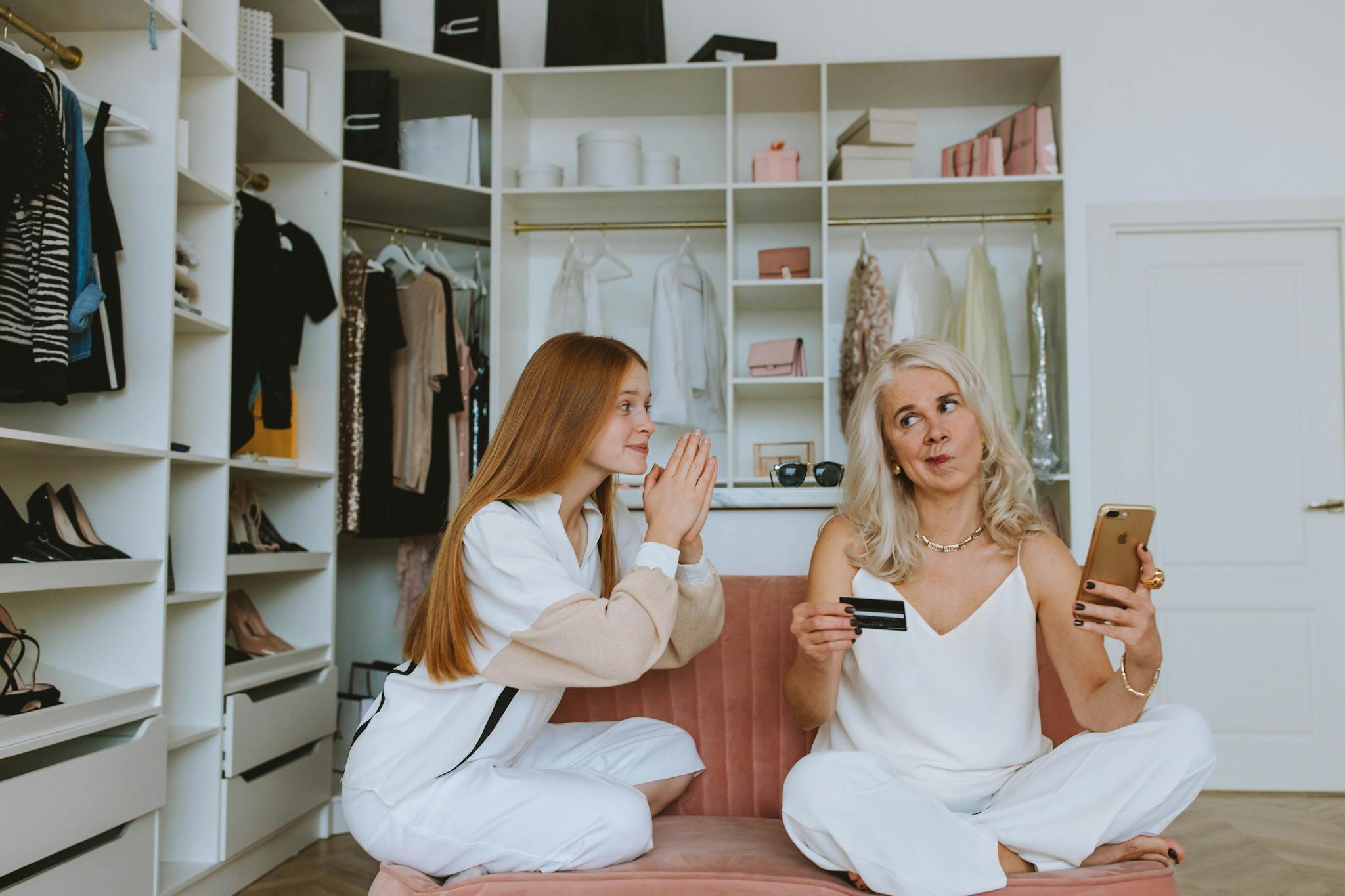 A senior woman and young woman shopping online with a credit card in a stylish wardrobe setting.
